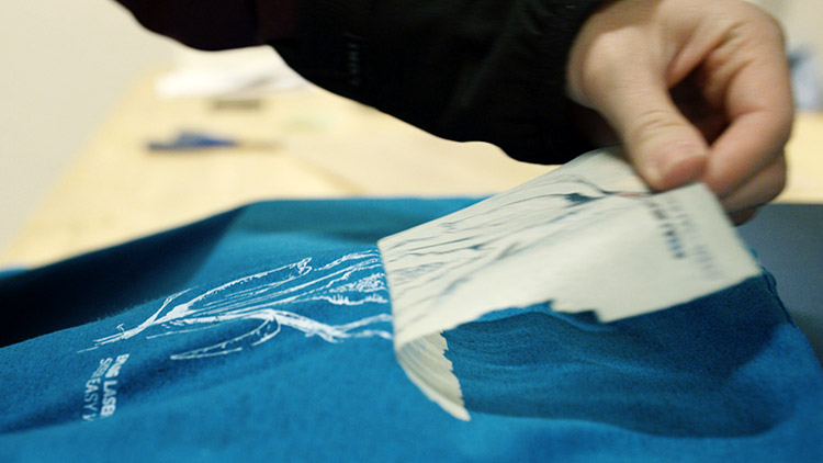 Peeling away the heat transfer material to reveal the heat-pressed design